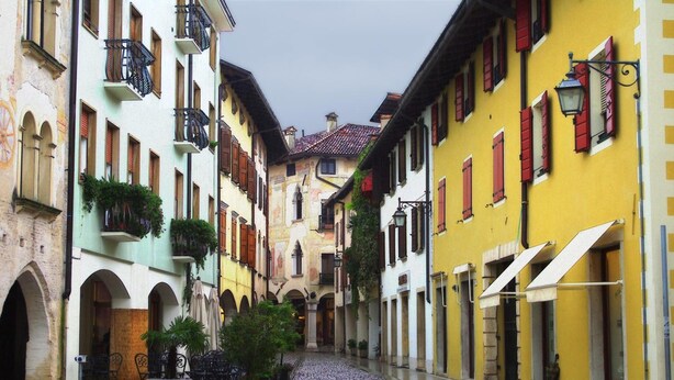 A narrow street with buildings on both sides, featuring balconies, awnings, and a cobblestone path. - Grand Hotel President (Spilimbergo)