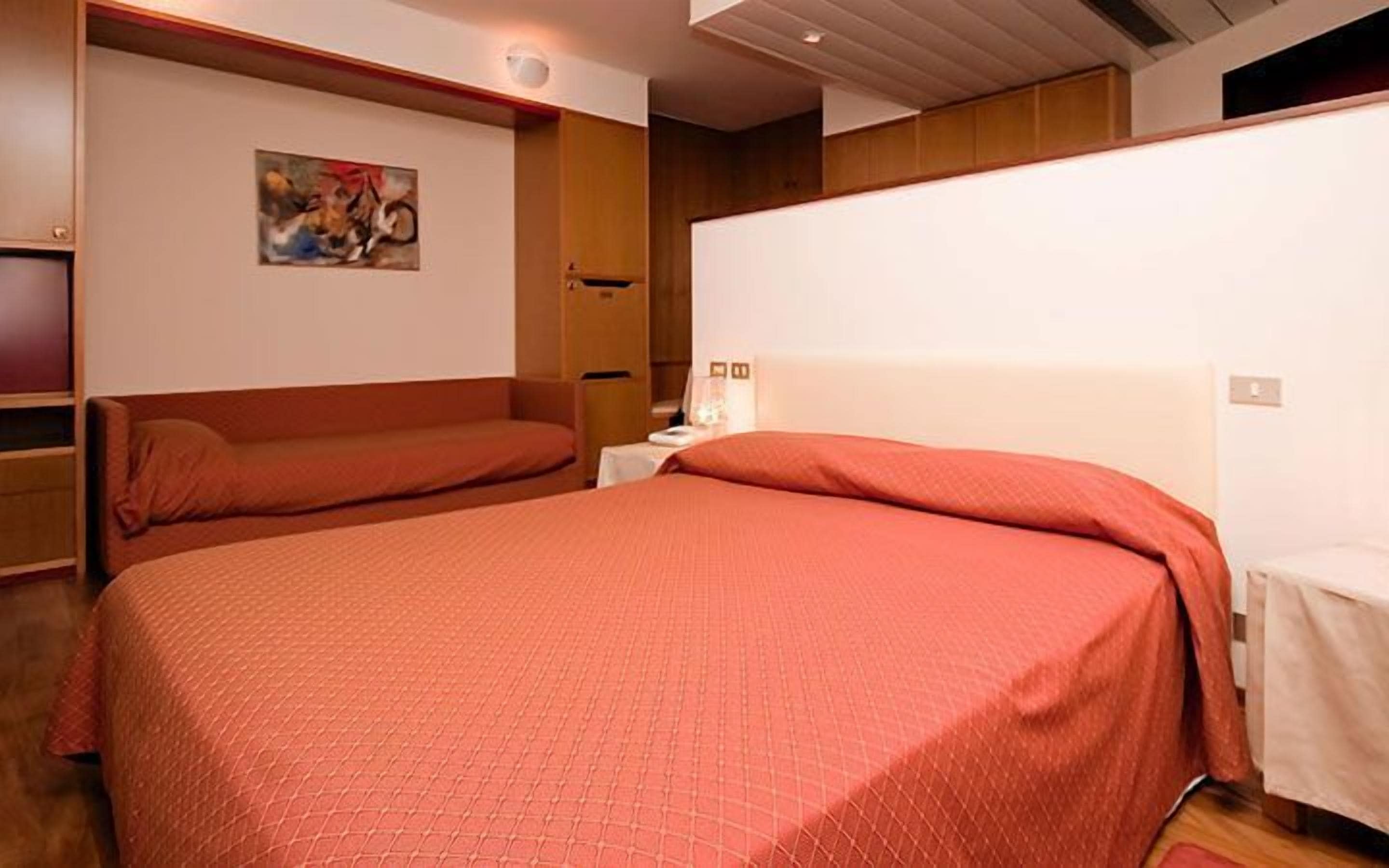 A hotel room with two beds, a painting on the wall, and a wooden headboard.