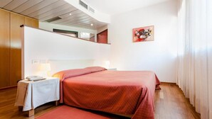 A hotel room with a bed, bedside table, lamp, and a red rug. - Grand Hotel President (Spilimbergo)