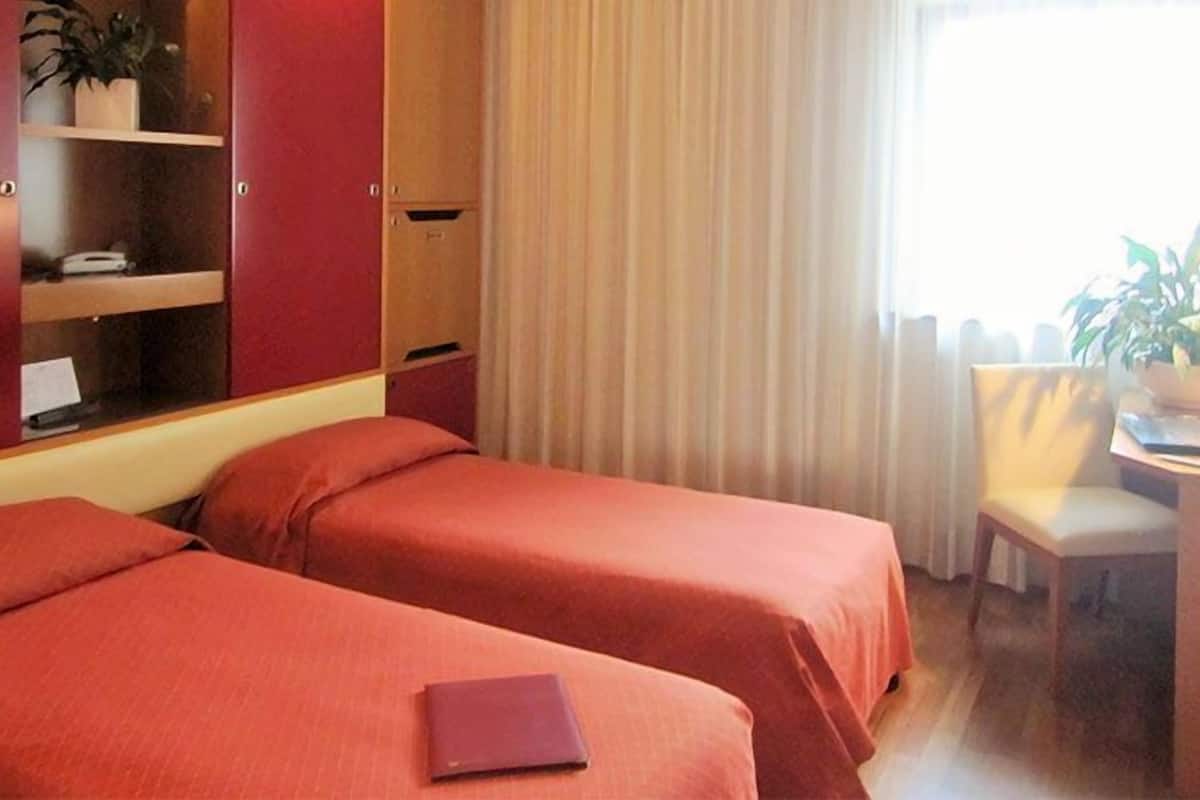 Ein Hotelzimmer mit zwei Betten, einem Schreibtisch, einem Stuhl und einem Fenster mit Vorhängen.