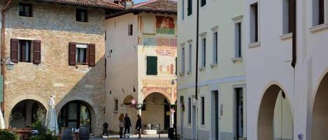 A cobblestone street with historic buildings, including a clock tower and an archway.