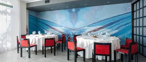 A dining area with round tables, red chairs, and a blue mosaic wall.