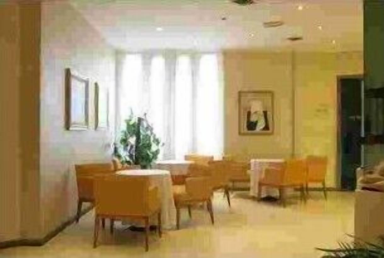 Un comedor de hotel con mesas y sillas redondas, un ventanal con cortinas y obras de arte enmarcadas en las paredes.