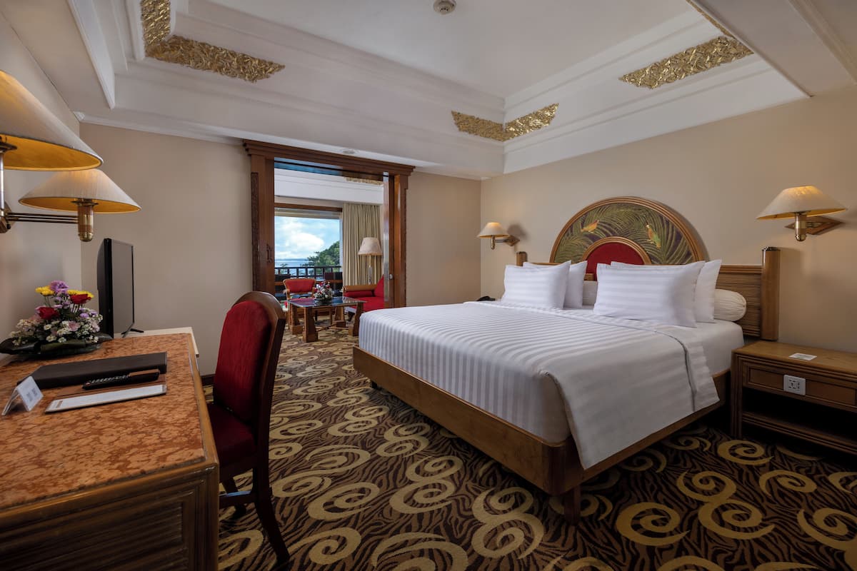 A hotel room with a large bed, a desk with a computer, a chair, and a view of the outside.