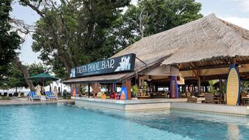Un bar junto a la piscina con techo de paja, sillones de descanso y una piscina cristalina.