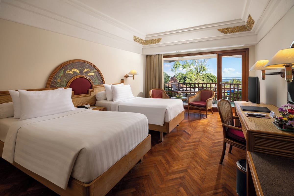 A hotel room with two beds, a desk, and a view of the outdoors.