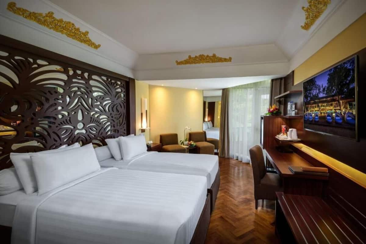 A hotel room with two beds, a desk, a TV, and a decorative wall.