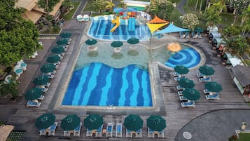 Relax by the resort's central pool, featuring a wave-like design, surrounded by lounge chairs and umbrellas.