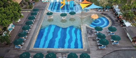 Vista aérea de un complejo turístico con un amplio área de piscina, numerosas tumbonas y sombrillas.
