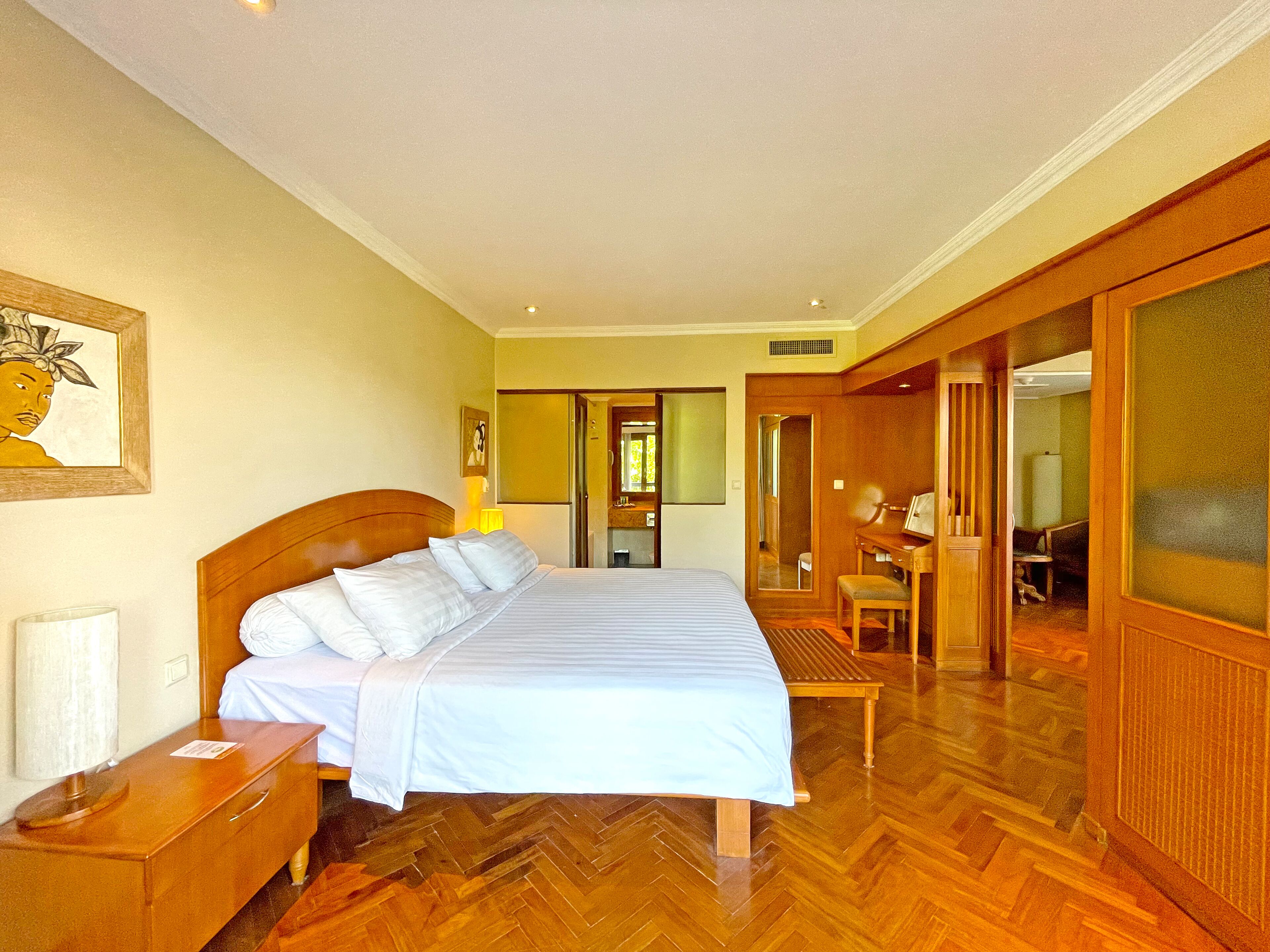 Een hotelkamer met een groot bed, een houten vloer, een bureau met stoel en een spiegel.