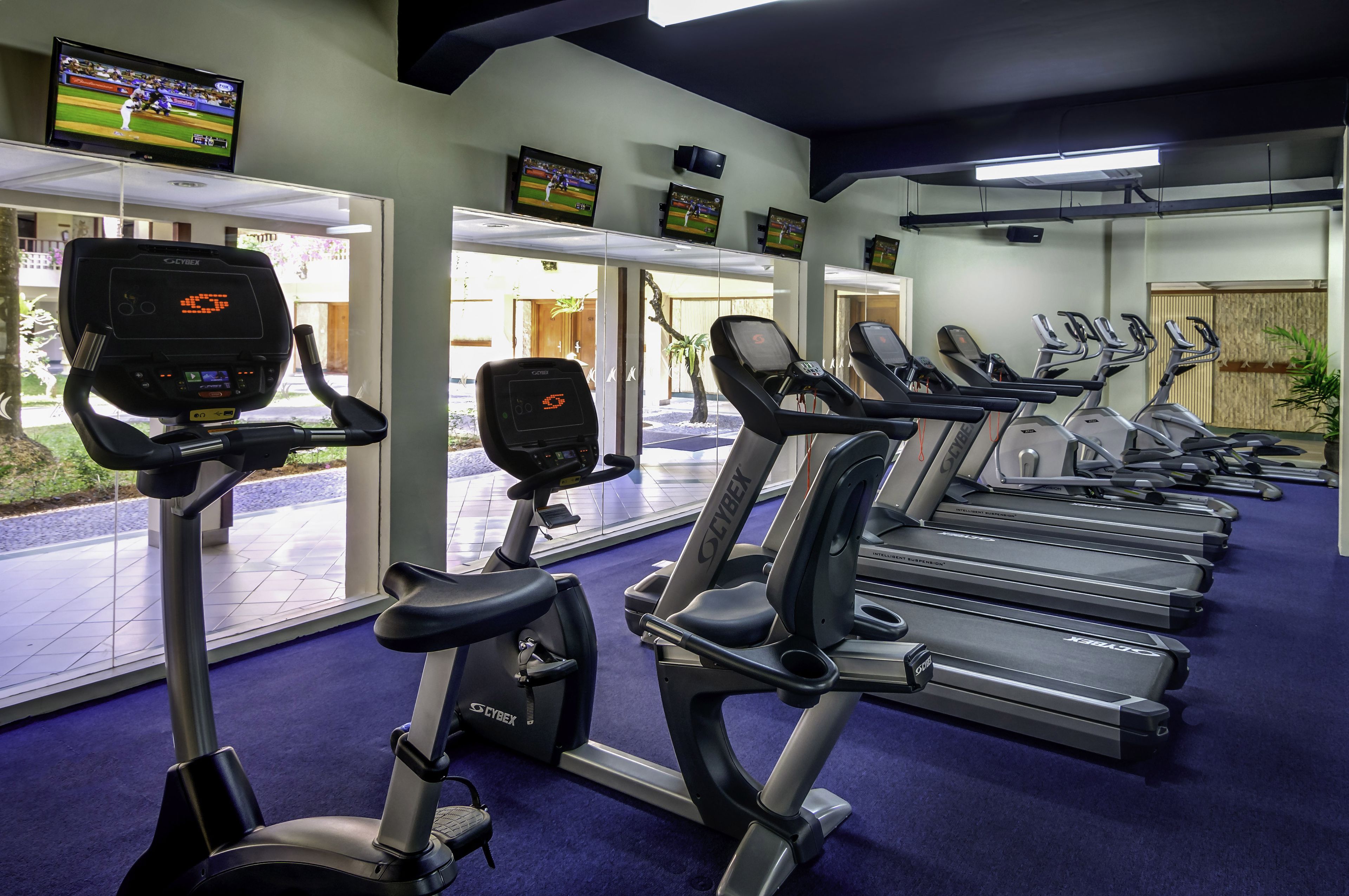 A gym with treadmills, stationary bikes, and a TV displaying a sports game.