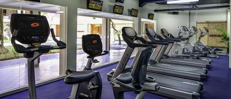 A gym with treadmills, stationary bikes, and a TV displaying a sports game.