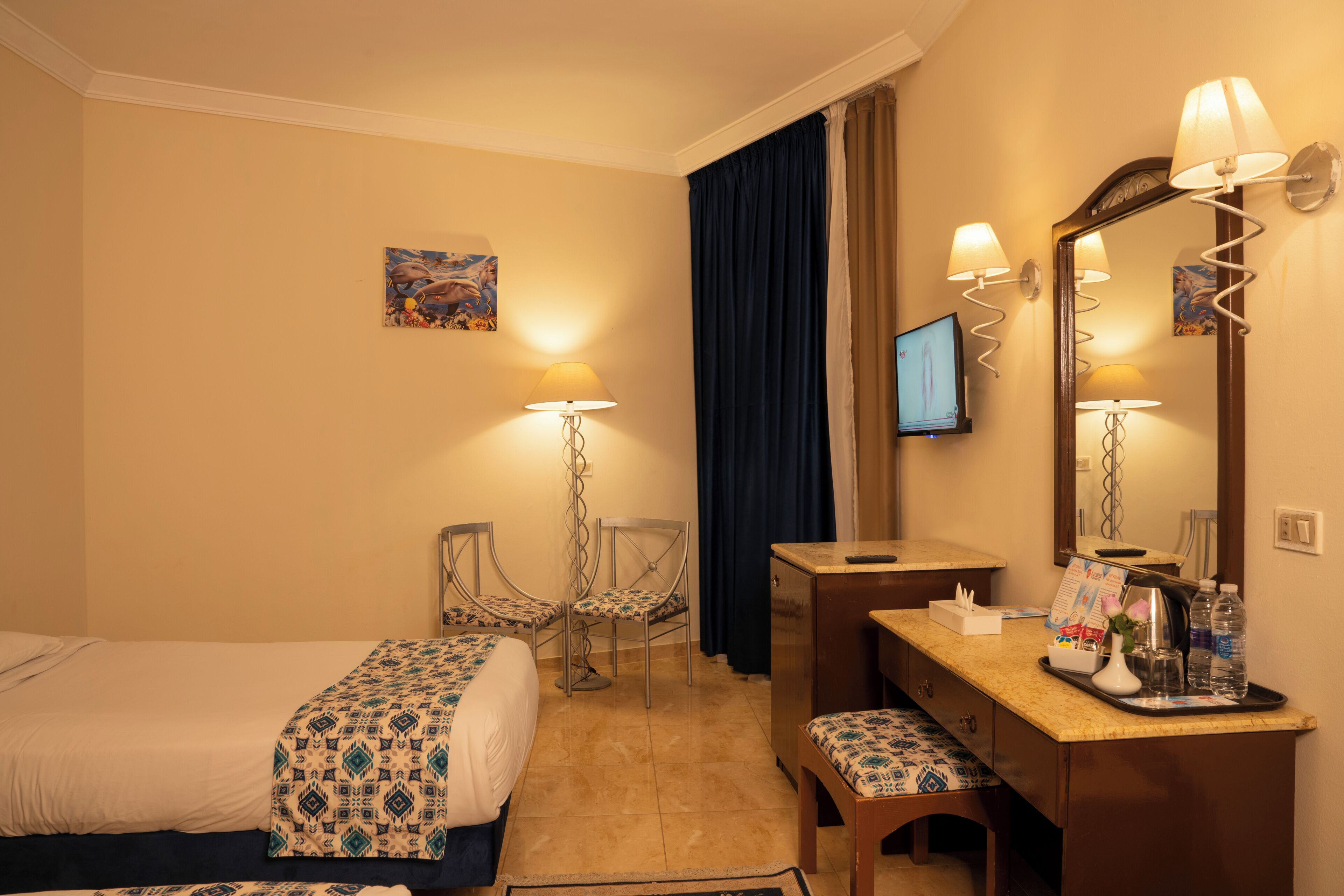 A hotel room with a bed, a desk, a chair, a TV, a mirror, and a window with curtains.