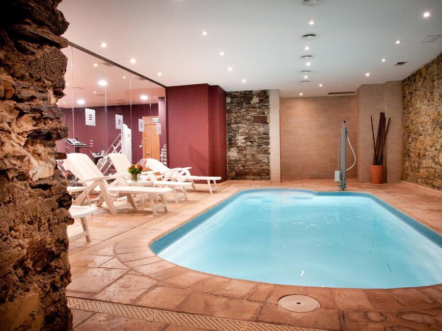 An indoor swimming pool with lounge chairs, a stone wall, and a glass partition.