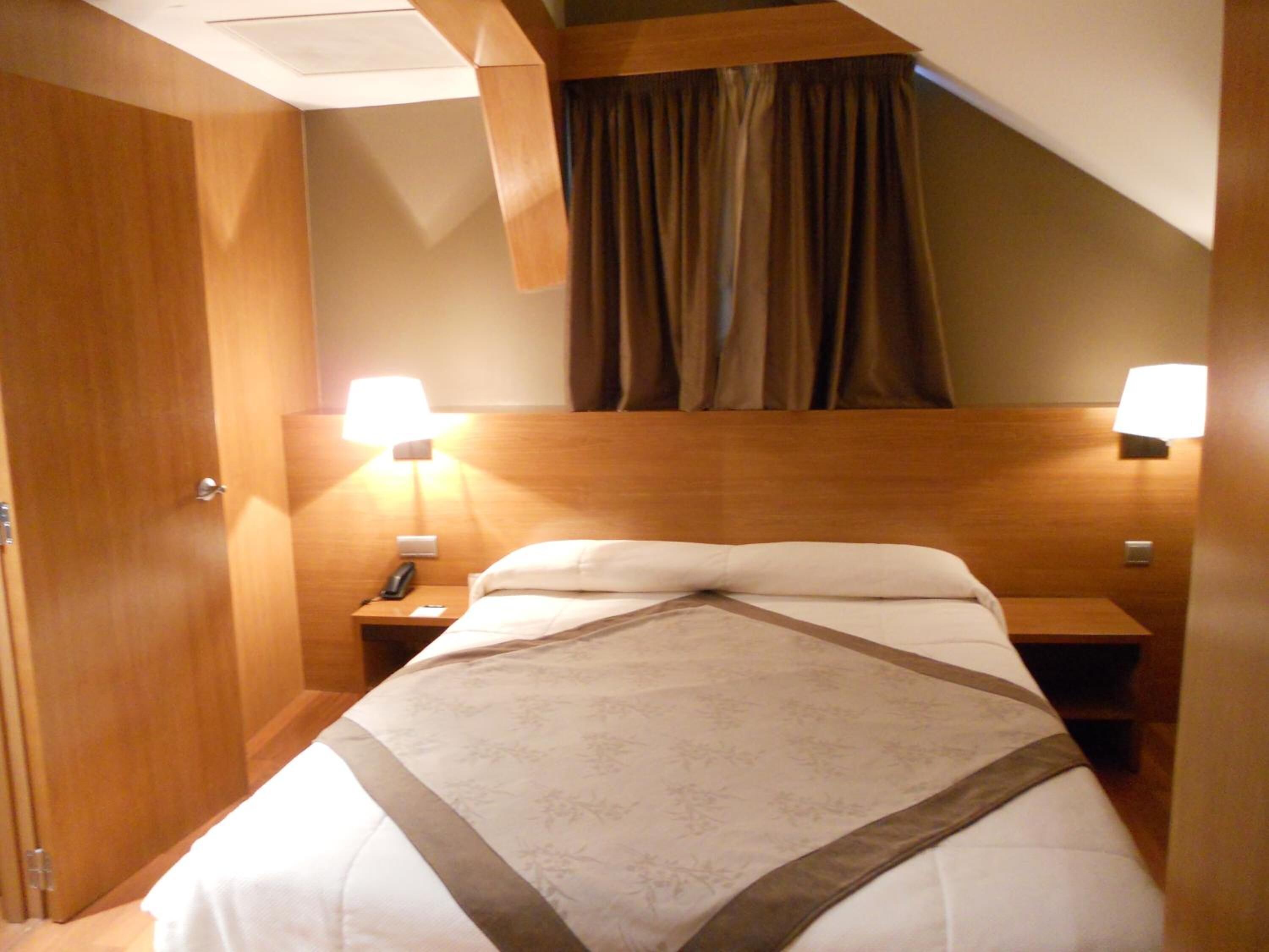 A hotel room with a bed, two bedside lamps, a telephone, and a wooden headboard.
