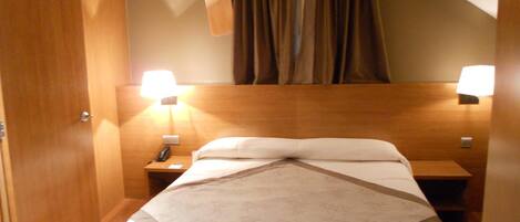 A hotel room with a bed, two bedside lamps, a telephone, and a wooden headboard.