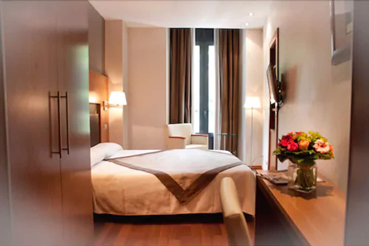 A hotel room with a bed, bedside table, lamp, and a vase of flowers.