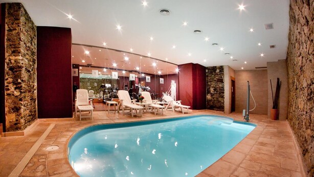 An indoor swimming pool with lounge chairs and a spa area.