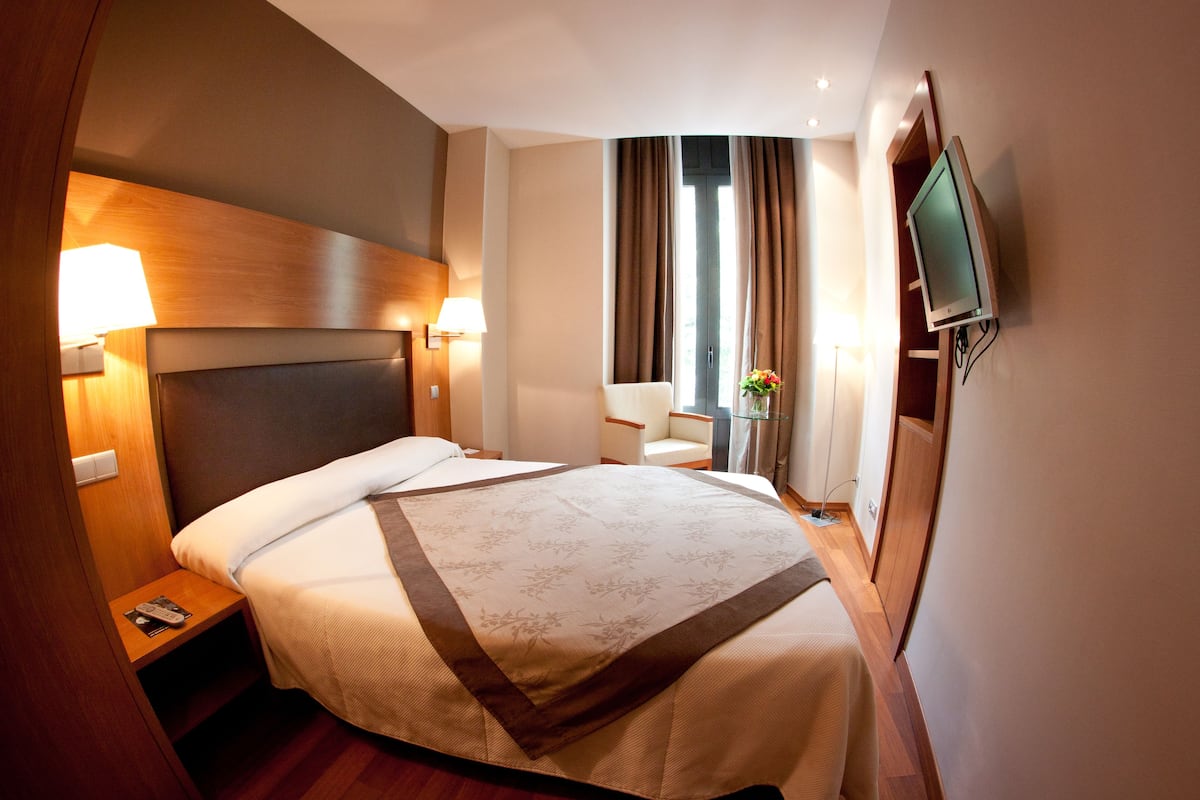 A hotel room with a large bed, bedside lamps, a TV mounted on the wall, and a window with curtains.