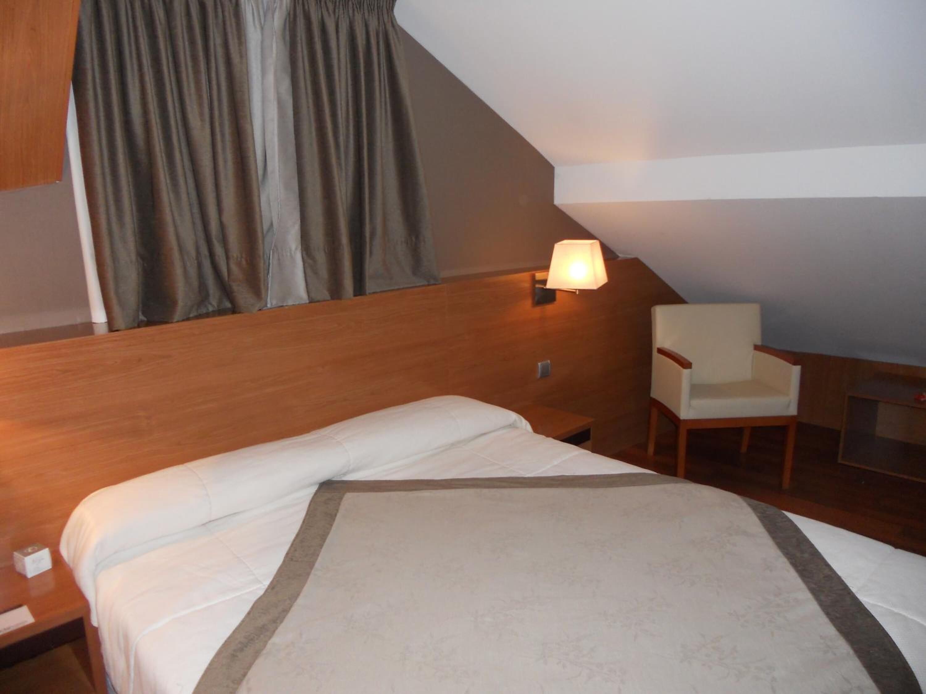 Una habitación de hotel con cama, una silla, una lámpara y una ventana con cortinas.