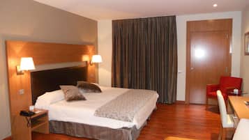 Una habitación de hotel con una cama grande, dos lámparas de noche, un escritorio con una silla y una silla roja.
