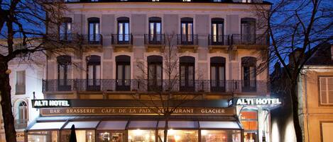 Un hotel de varios pisos, con balcones y diversos comercios en la planta baja, incluyendo un bar y un restaurante.