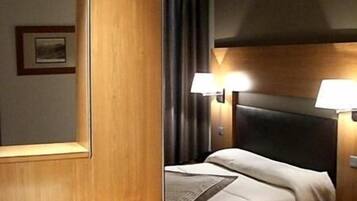 A hotel room with a wooden headboard, a bed with white linens, a nightstand with a lamp, and a desk with a chair.
