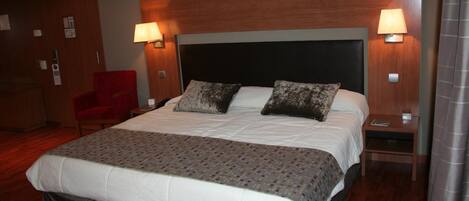 A hotel room with a large bed, two bedside lamps, a red chair, and a wooden headboard.