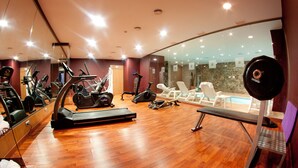 A gym with exercise equipment, a bench, and a view of a pool through glass walls.