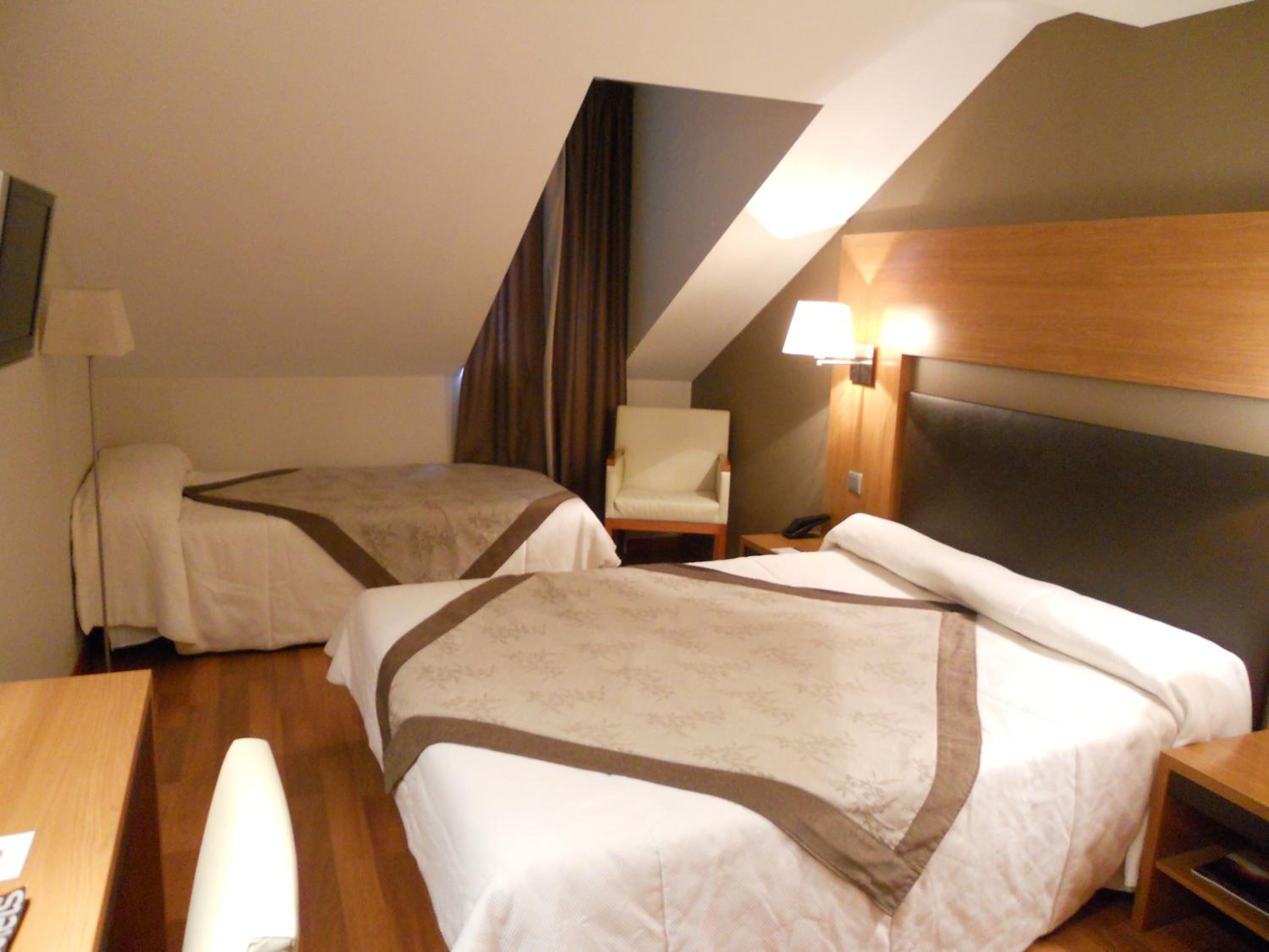 Une chambre d’hôtel avec deux lits, un bureau et une chaise. Il y a une lampe sur le bureau et un téléphone sur la table de chevet.