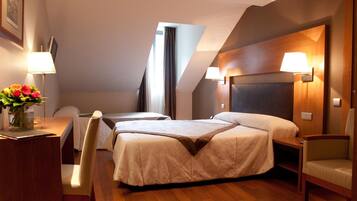 A hotel room with two beds, a desk, a chair, and a lamp.