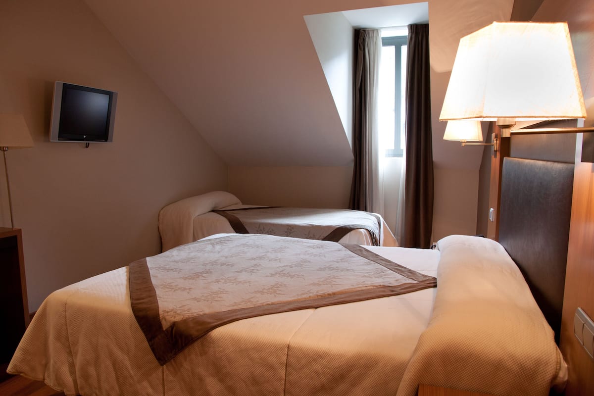 A hotel room with two beds, a television, a lamp, and a window with curtains.