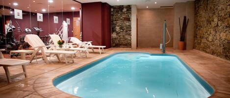 Una piscina interior con sillones de descanso y equipo de ejercicio.