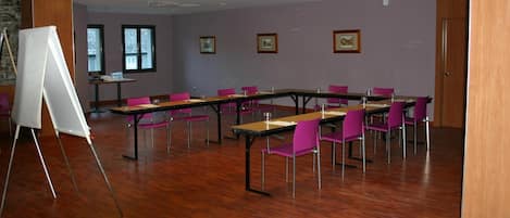 Un salón de conferencias con mesas de madera y sillas moradas, una pizarra blanca y cuadros en la pared.