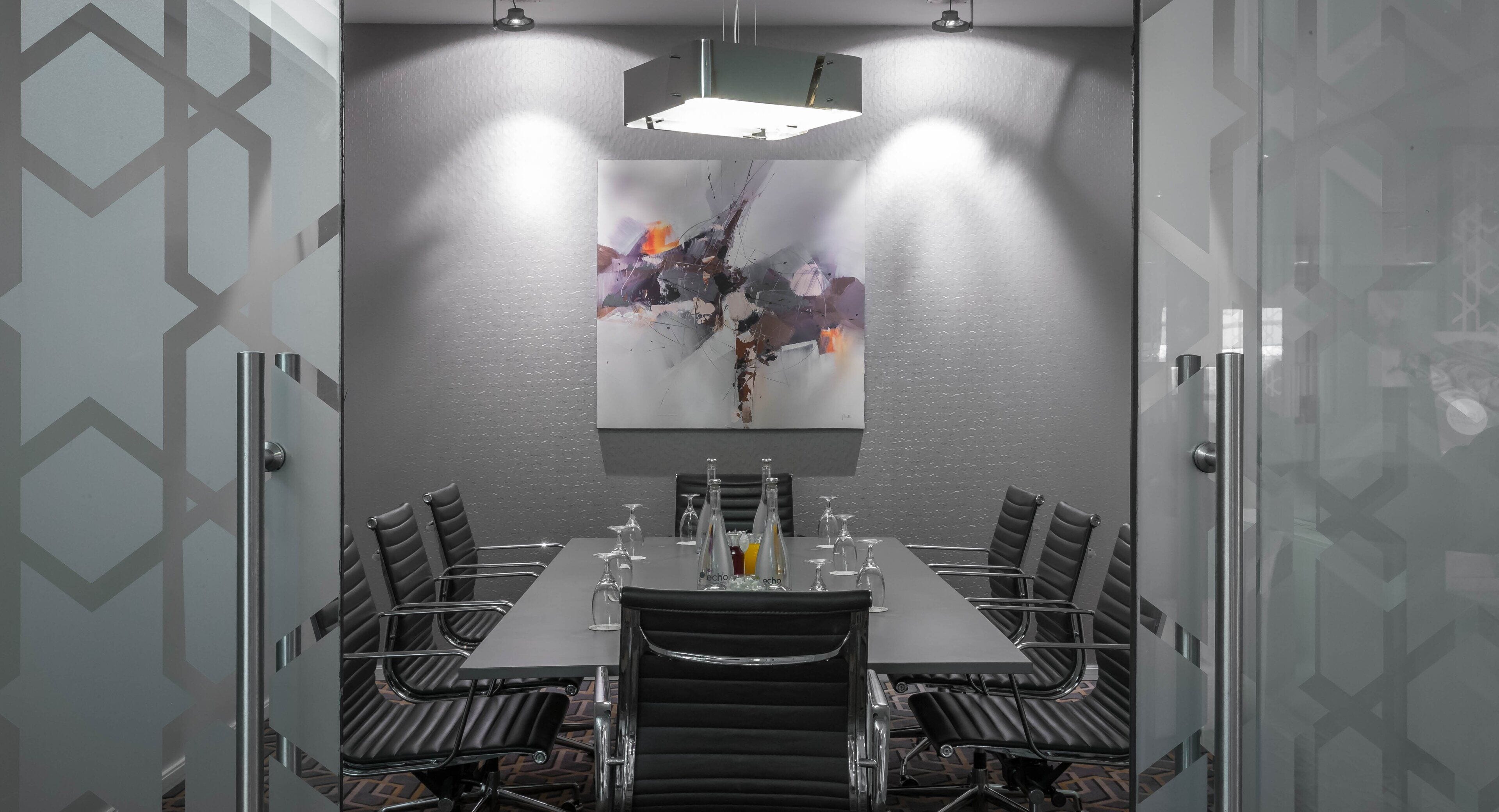 A conference room with a long table, black leather chairs, and a modern abstract painting on the wall.