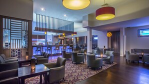 Een moderne hotellobby met een bar, zitgedeeltes en een kamerbreed tapijt.