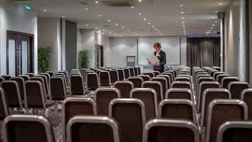 Un salón de conferencias con filas de sillas, un atril y una pantalla para presentaciones.