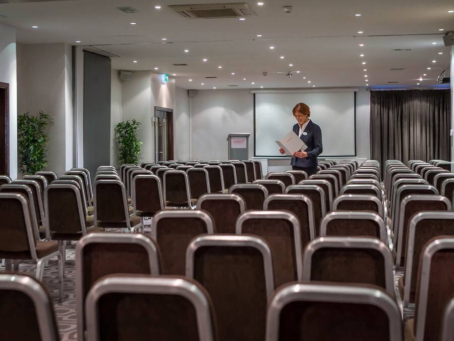 Un salón de conferencias con filas de sillas, un atril y una pantalla para presentaciones.