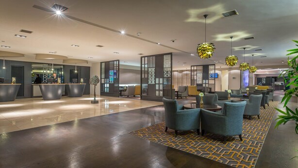 Een moderne hotellobby met een receptiebalie, zithoek en decoratieve elementen.