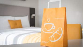 Una habitación de hotel con una cama, una mesita de noche y una mesa con un paquete de café.