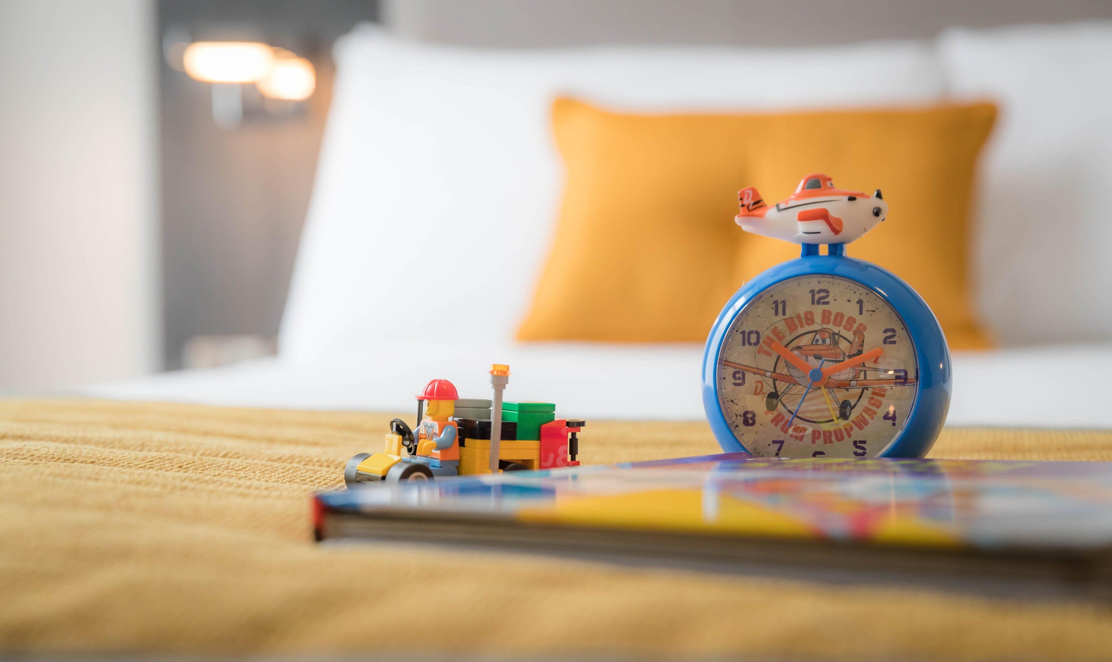 Una cama con un despertador azul, un juego de construcción infantil y un libro sobre una superficie de madera.