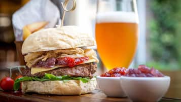 Een hamburger met een cocktailprikker, een glas bier en twee kleine schaaltjes saus op een houten tafel.