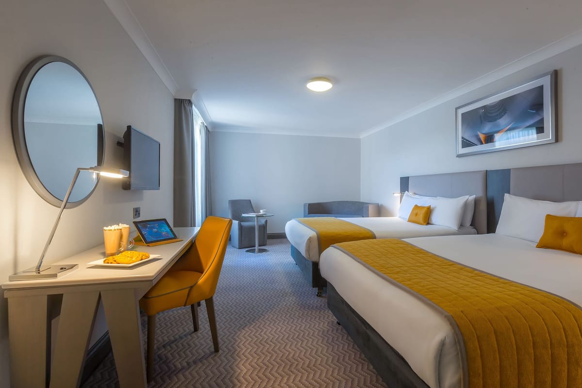 Une chambre d’hôtel avec deux lits, un bureau avec une chaise, une télévision et un grand miroir.