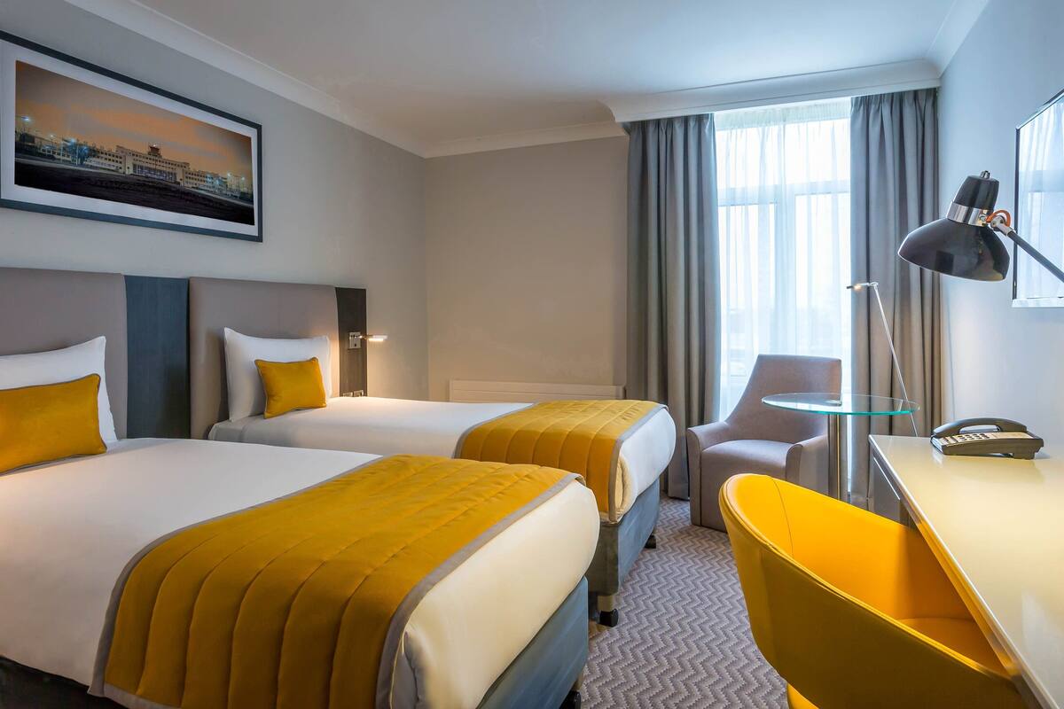 Une chambre d’hôtel avec deux lits, un bureau, une chaise, une lampe et un téléphone.