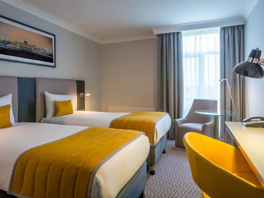 A hotel room with two beds, a desk, a chair, a lamp, and a telephone.