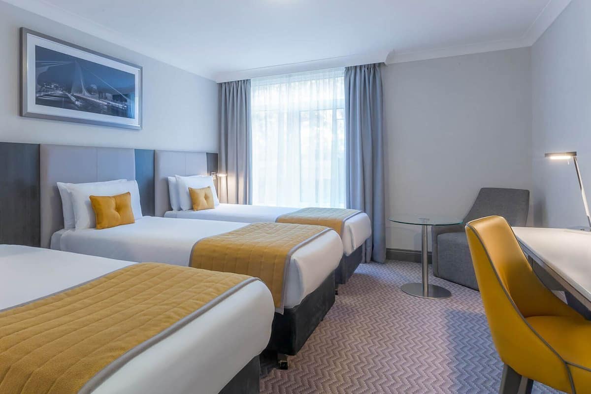 Une chambre d’hôtel avec trois lits, un bureau et une chaise.