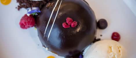 A dessert with chocolate and ice cream on a white plate with berries and chocolate shavings.
