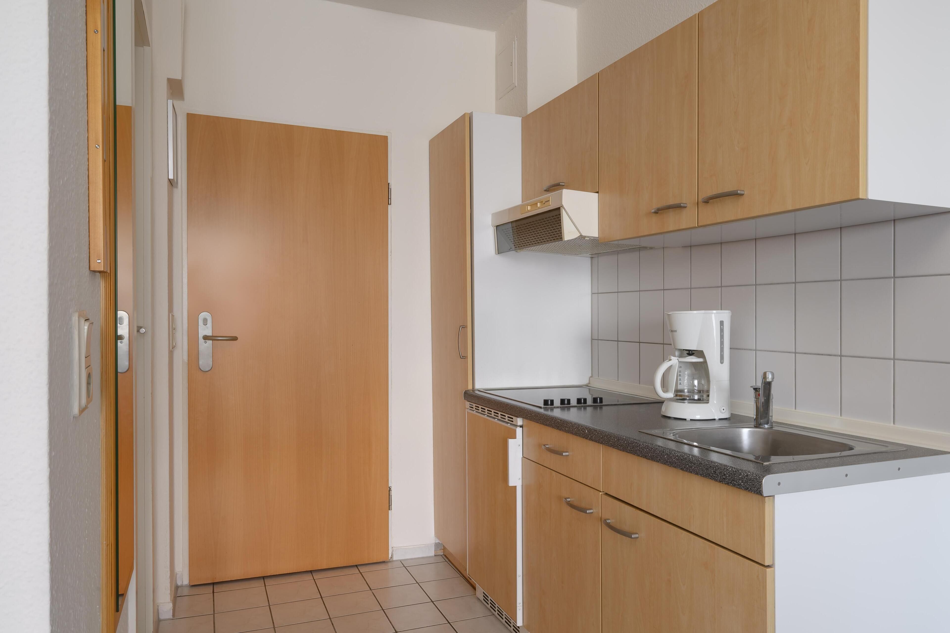Una cocina compacta con armarios de madera, microondas integrado y cafetera.