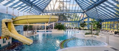 Una piscina interior con tobogán, sillones reclinables y techo de cristal.