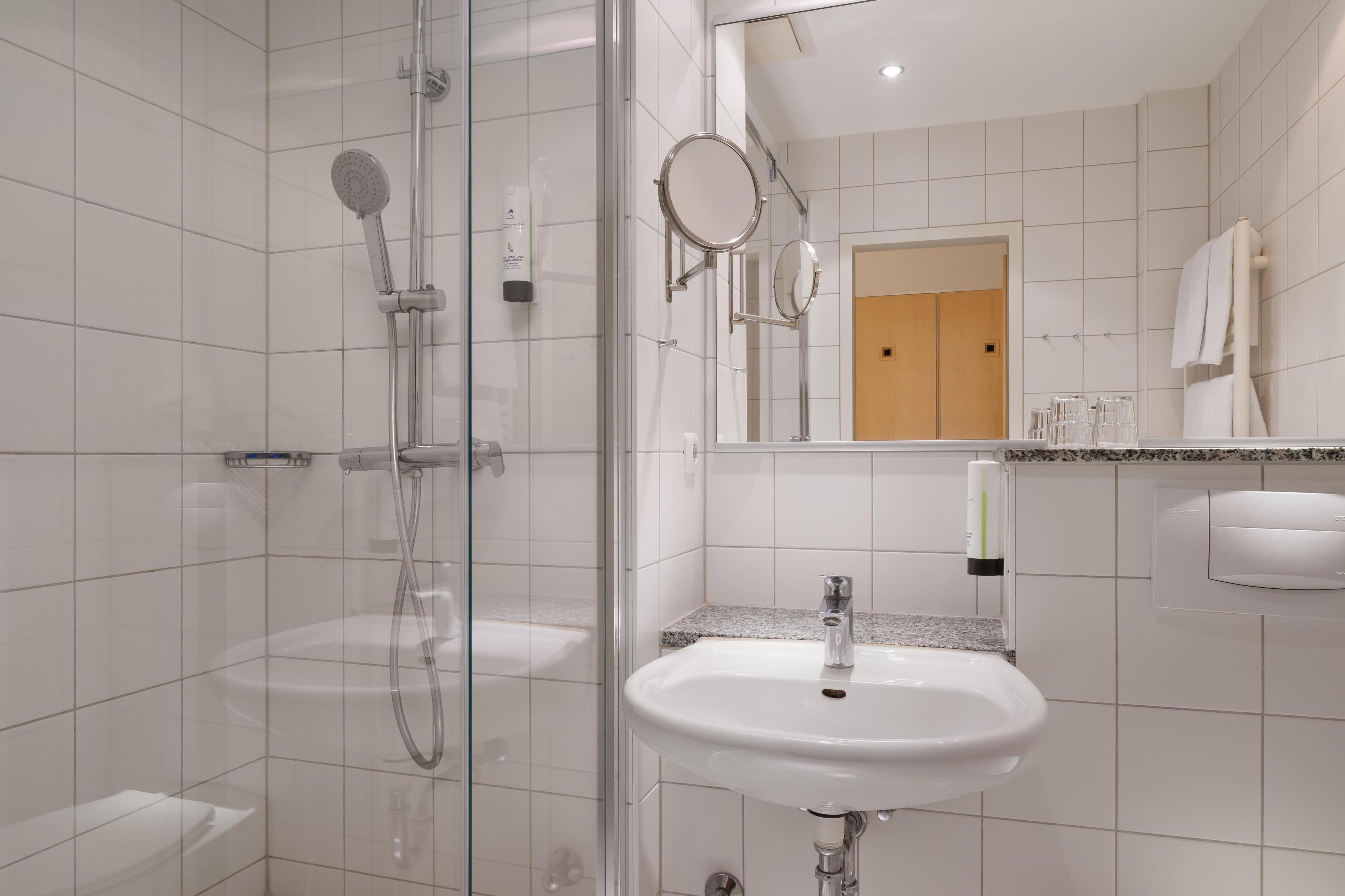 A modern bathroom with a glass-enclosed shower, a white sink, and a mirror.